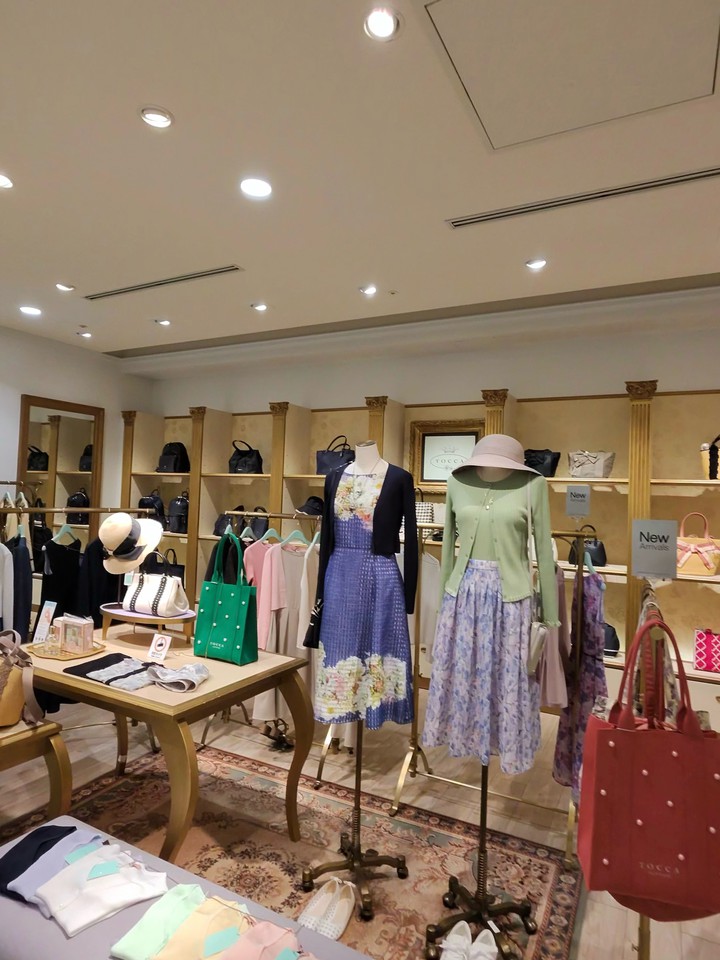 明るく広々としたTOCCAショップの店内。さまざまな春のドレスやアクセサリーが展示され、中央のテーブルには色とりどりのバッグが並んでいる