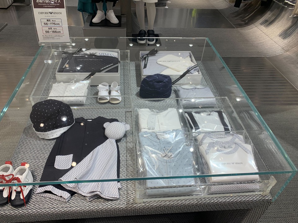 エンポリオアルマーニジュニアの店内ディスプレイケースに展示されている高級子供服。黒と白の色合いで統一されたスタイリッシュな服と帽子、靴が見えます。