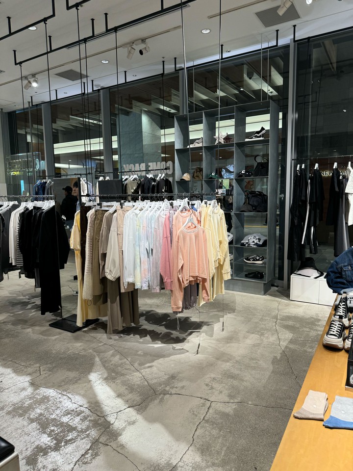 明るいコンバーストウキョウの店内で、多様な色合いの衣服が陳列されている様子です。