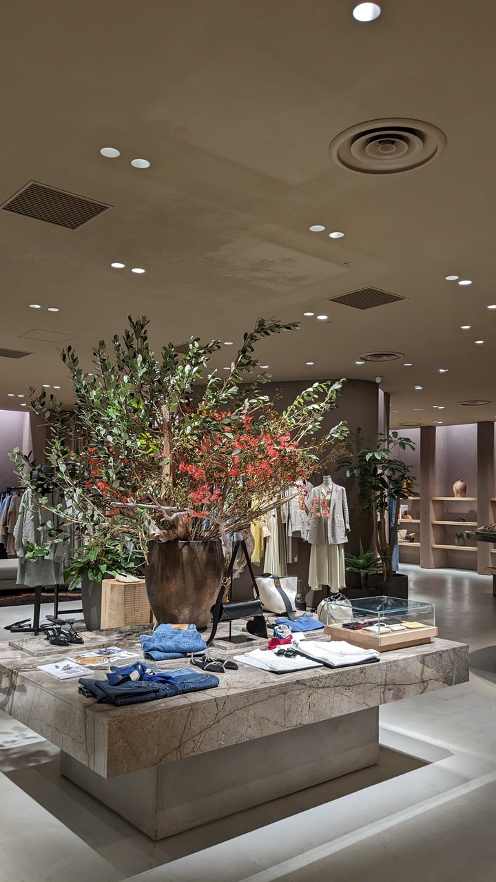 カオス店内に飾られた大きな植物と商品が展示された大理石のテーブル。背景には洋服が掛けられており、店内の明るい照明が雰囲気をつくりだしています。