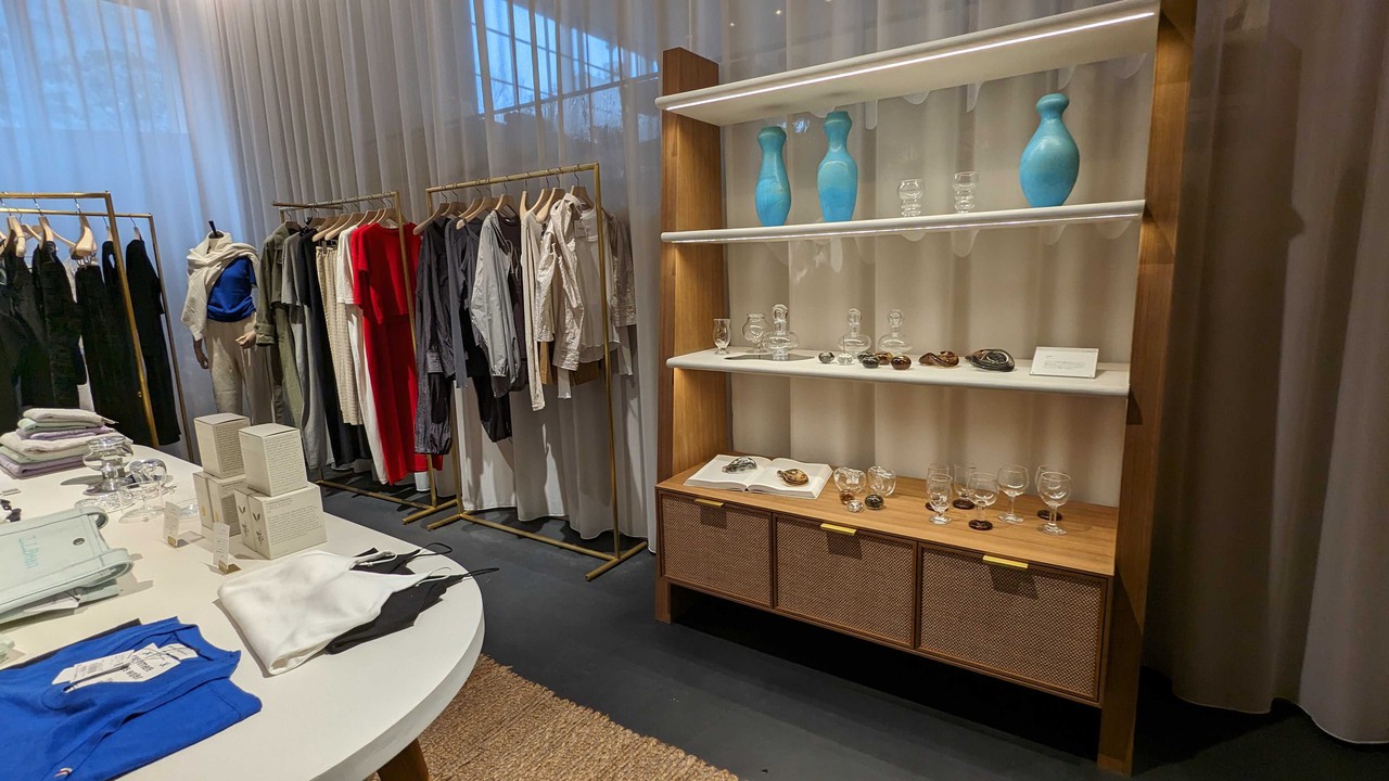 サロン アダム エ ロペ店内壁面の棚には青い花瓶やガラス製品が並び、その周囲には服やアクセサリーがディスプレイされています。