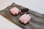 波模様の黒いお皿に、2つのピンク色の亀の形をした和菓子と、小さな黒い器に盛られた黒い餡が並んでいる。亀の和菓子は可愛らしく、伝統的な和の雰囲気を感じさせる画像。