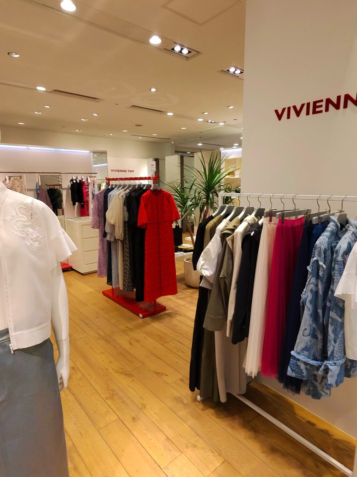 木のフローリングと白い壁が特徴的なVIVIENNE TAMの店内。壁にはブランド名が記され、マネキンと衣服がラックに陳列されており、落ち着いた雰囲気の中でさまざまなスタイルの服が展示されている。