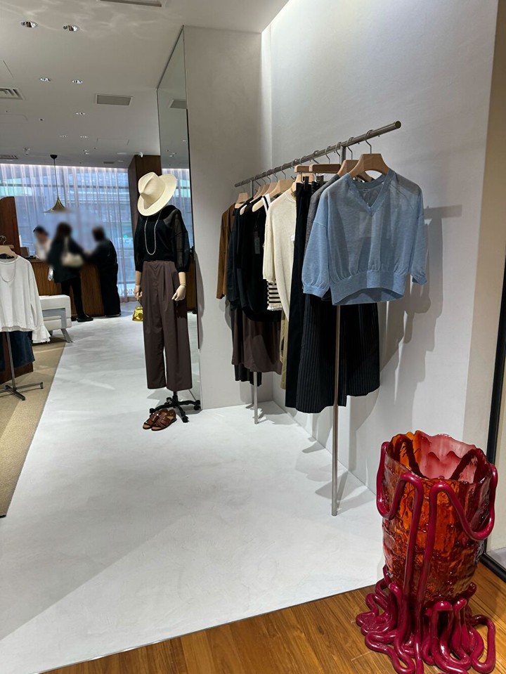 「BRILL」のモダンな店内で、ハンガーにかけられたトレンディな衣類と装飾的な花瓶。