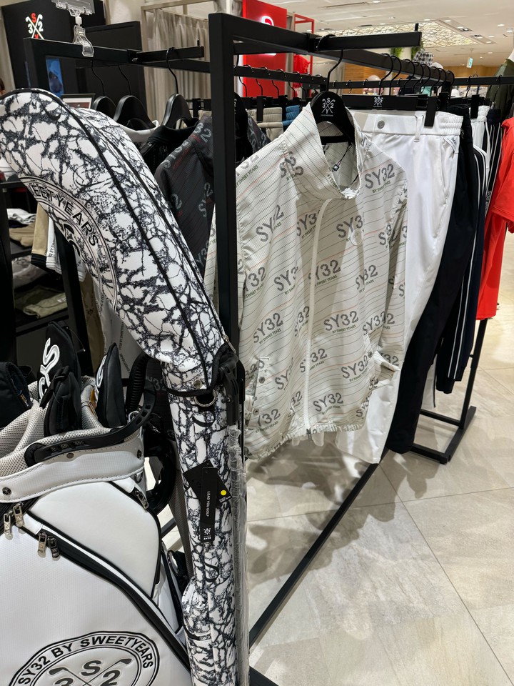 SY32 by SWEET YEARS GOLFの店内には、模様入りのゴルフバッグとブランドロゴ入りの白いゴルフウェアがあり、おしゃれなゴルフスタイルを提案しています。