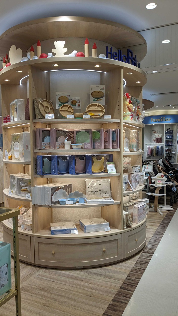 新宿高島屋ハローベビーサロン 子供用のお皿やカトラリー、ビブなどの食事用品が展示されたコーナー。木製の棚には青やピンク、緑の食器が並ぶ。
