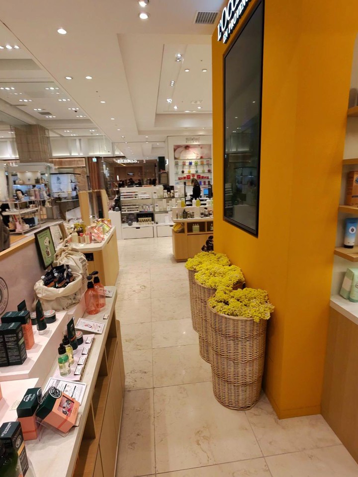 ロクシタン店内の通路に黄色い花が飾られ、横に商品も並んでいる