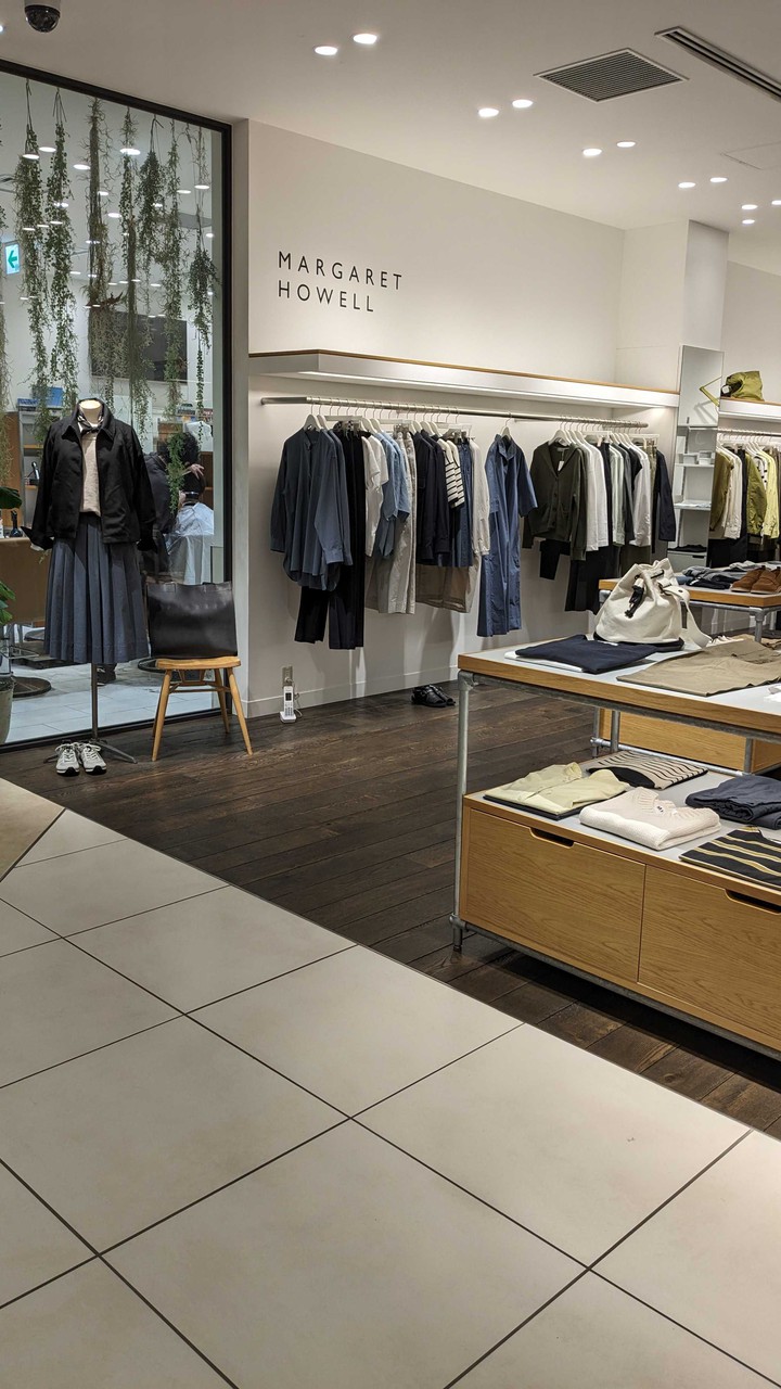 マーガレットハウエルの店内で、モノトーンの衣服が並ぶ洋服ラックとシンプルなデザインの家具が配置されています