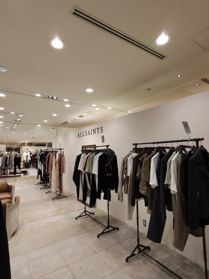 ALLSAINTSの店内で、天井にはスポットライトが並び、フロアにはさまざまなスタイルのジャケットとトップスが掛かったラックが並んでいる。