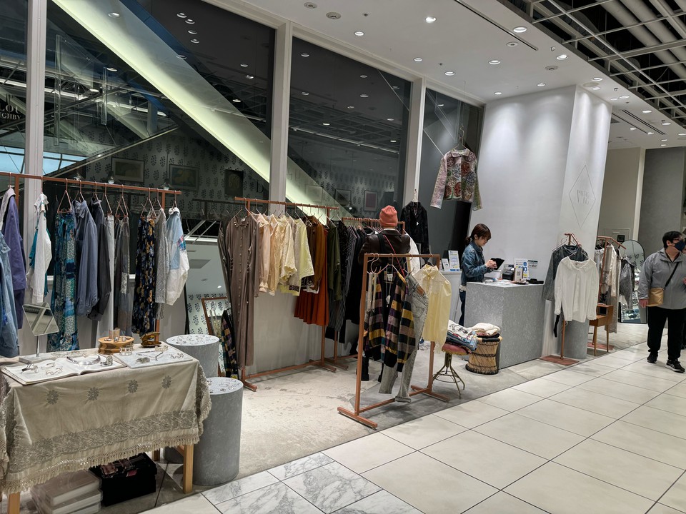ザヴィンテージングの店内には、さまざまなスタイルの衣服が掛けられたラックがあり、中央のテーブルにはアクセサリーが展示されています。
