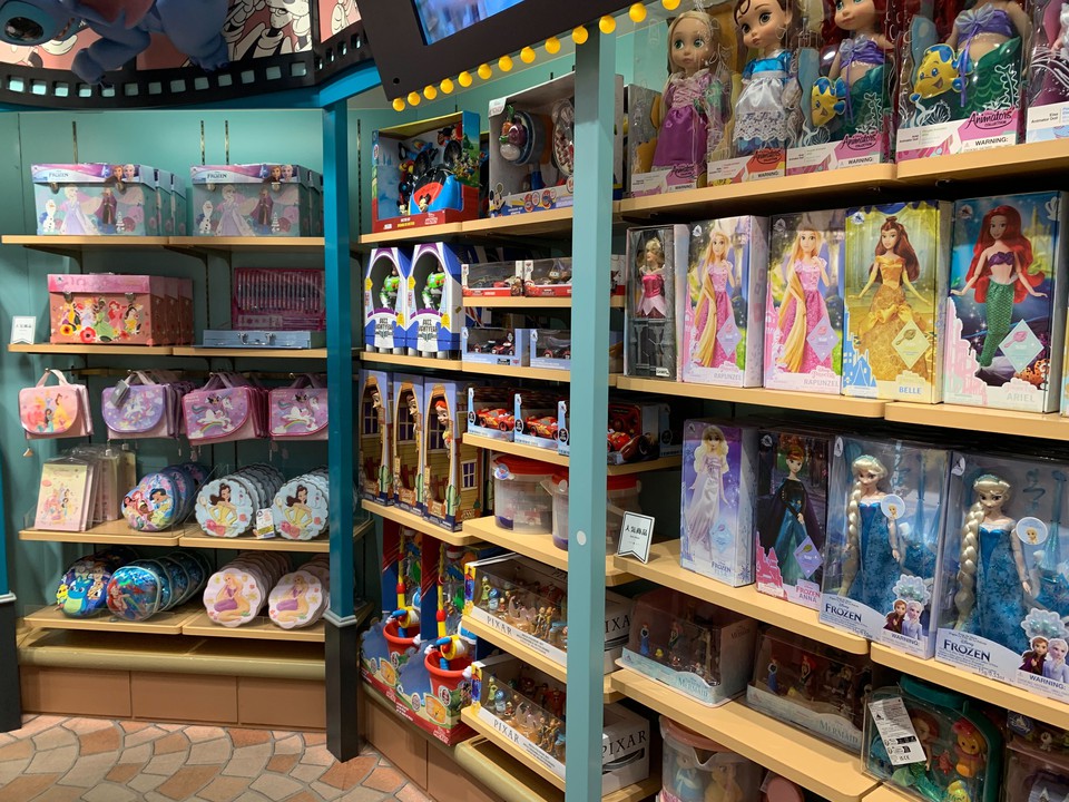 Disney storeでディズニープリンセスの人形やその他のキャラクターグッズが棚に色とりどりに並べられた棚