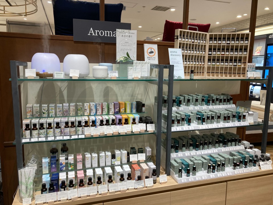 「Aroma」の看板の下、アロマオイルとディフューザーが陳列されたヘルスコンシャスラボのアロマコーナー。リラックスや気分転換に適した商品がそろっています。