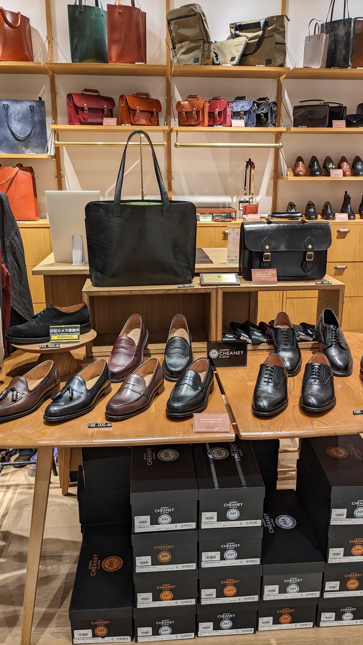 ブリティッシュメイドの店内で展示されている多様なメンズレザーシューズのコレクション。テーブルの上には、黒と茶色の靴が棚に整然と並べられています。