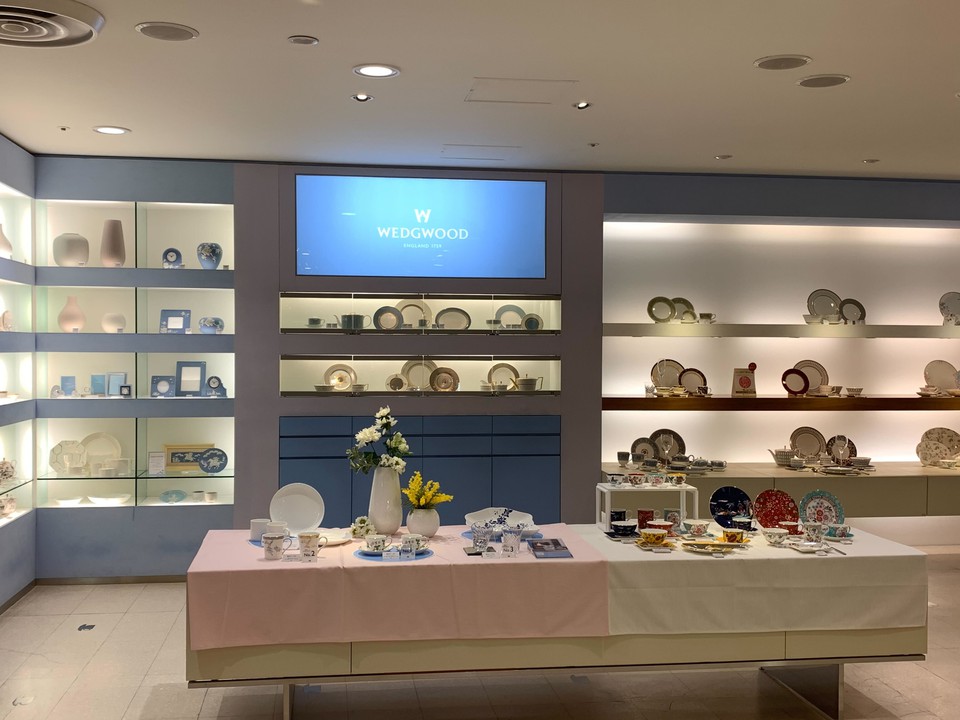 ウェッジウッドの店内で撮影された写真。壁の棚にはエレガントな食器が整然と並べられている。前面のテーブルには白い花瓶に挿された花と共に、さまざまな食器が展示されている。