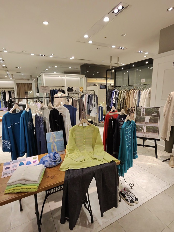 春のコレクションが展示されたアパレルショップ。手前にはライムグリーンのジャケットとチャコールグレーのパンツがディスプレイされており、背景には鮮やかなブルーの衣服が並んでいる