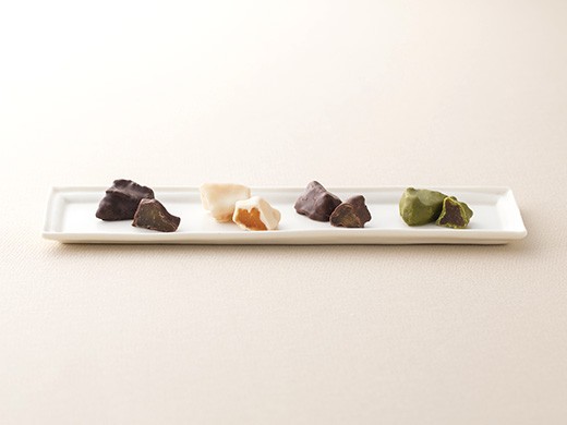 白い長方形のお皿に、さまざまな色のチョコレートでコーティングされた複数の種類のお菓子が並んでいる。シンプルで上品な配置が印象的で、上質なお菓子が提供される様子を伝えている画像。