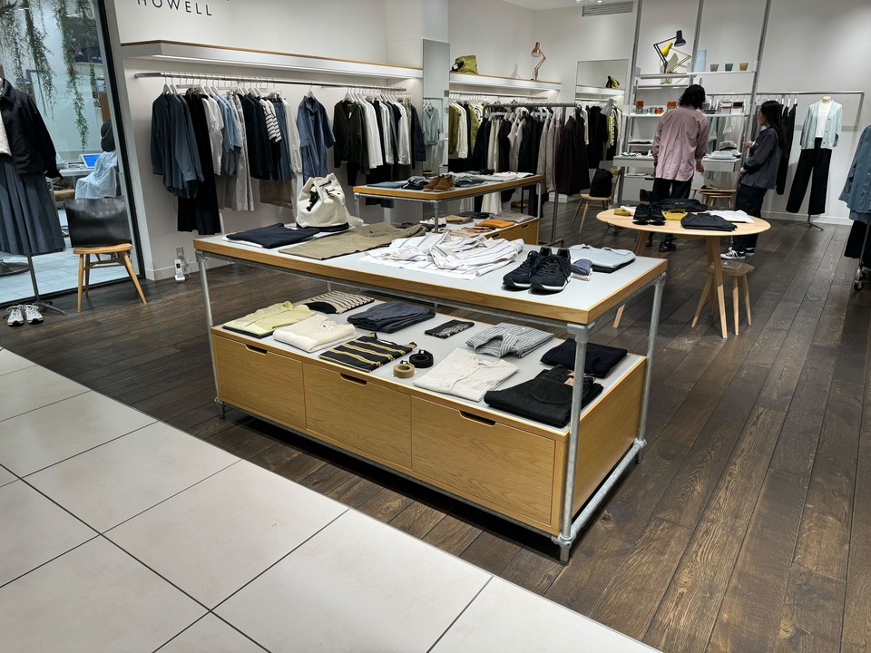 マーガレットハウエルの店内、木目調の床とモダンなデザインの衣料品が展示されたセンターテーブル。