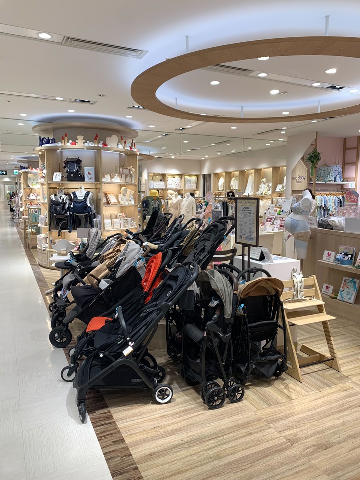 新宿高島屋ハローベビーサロン さまざまなデザインとサイズのベビーカーが並んだ売り場。奥にはベビーキャリアの棚も見える。