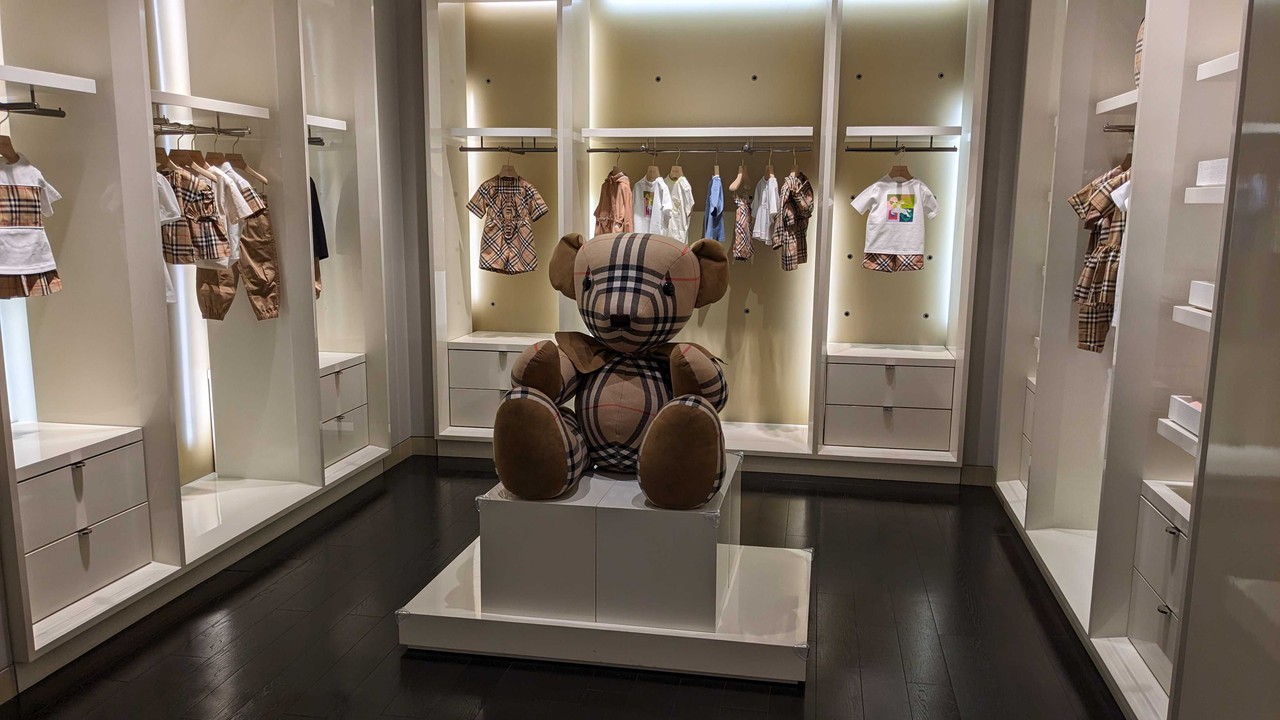バーバリーチルドレンの店内の様子。中央には大きなチェック柄のテディベアが展示され、周りの壁面ショーケースには同じチェック柄をあしらった子供服が並べられています。シンプルで上品な内装がブランドのイメージを際立たせています。