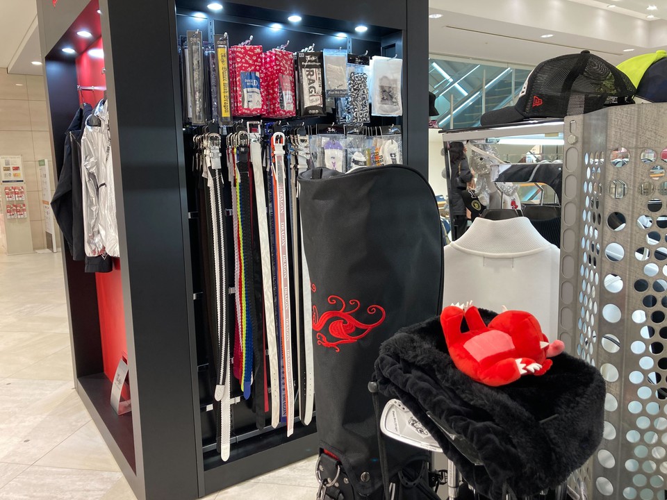店内のゴルフアクセサリーが並ぶコーナー。特徴的なブランドロゴのヘッドカバーと色とりどりのゴルフベルトが見えます。