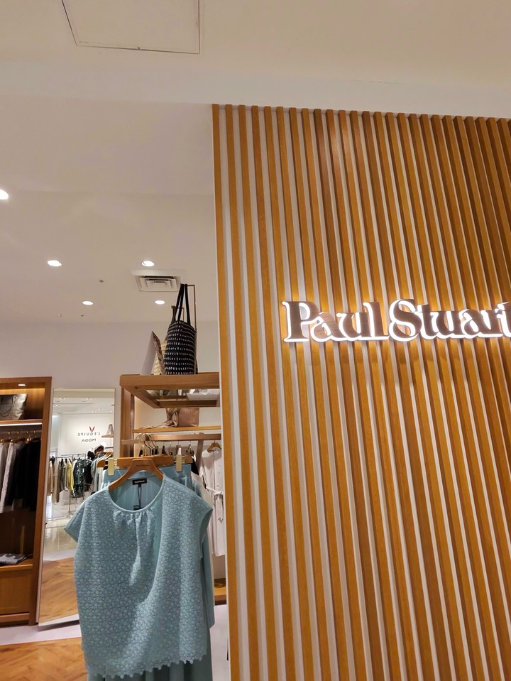 Paul Stuartのロゴが光る木製の装飾でできた壁、服が掛けられている