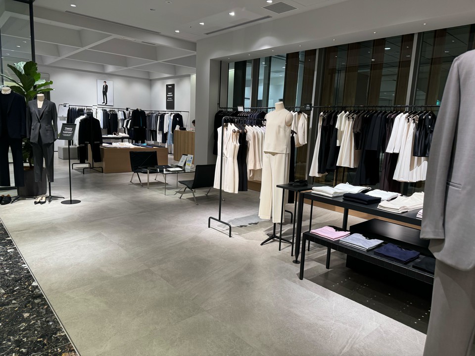 明るく広々としたセオリーの店内で、モダンなファッションがディスプレイされている。マネキンがシックなスーツを着用し、ラックにはモノトーンの衣服がきれいに並んでいます。