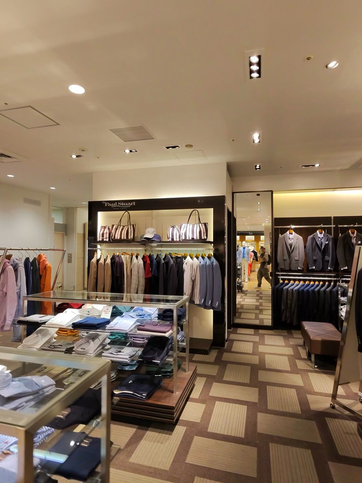 洗練されたPaul Stuart の店内で展示されるさまざまな色のメンズシャツとスーツ