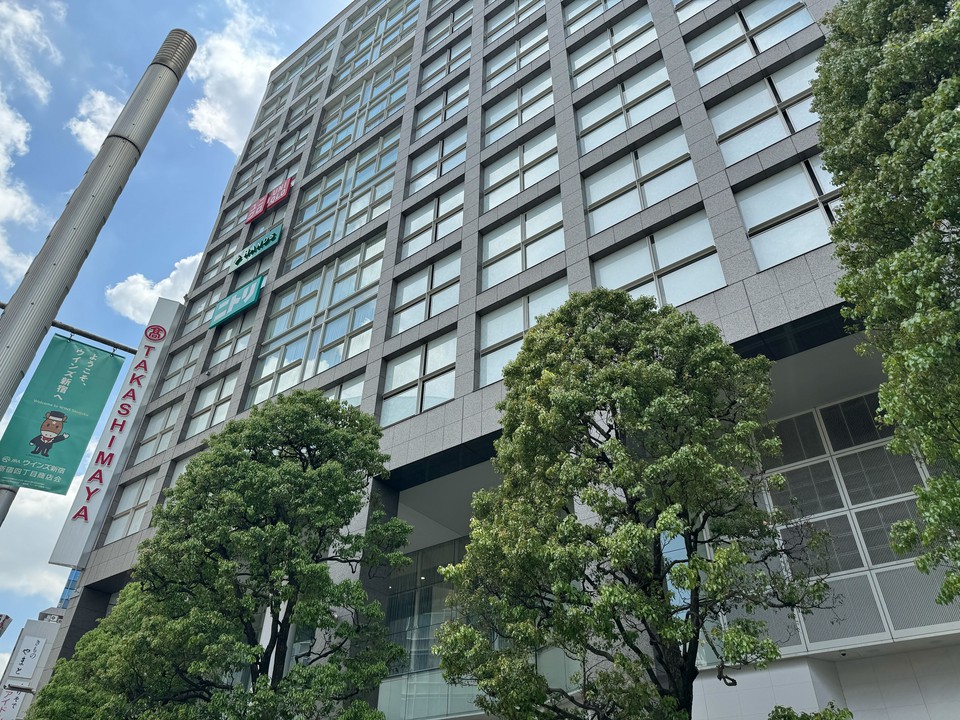 高層ビルに囲まれた緑溢れる歩道とTakashimayaの看板